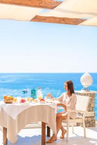Una donna seduta a un tavolo di fronte all'oceano di Hotel Ferdinando Beach & Thermal Spa a Ischia