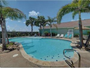 a swimming pool with palm trees and a house at Barefoot Bungalow - Pet Friendly- 2 Bdrm Townhome in Corpus Christi