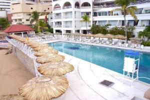 a swimming pool with straw umbrellas and chairs and a hotel at Romantic Suite w/Beach in Heart of Acapulco in Acapulco