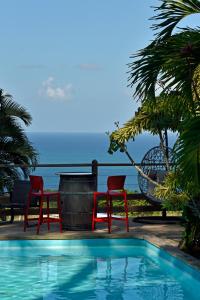 een zwembad met twee stoelen en een tafel naast de oceaan bij Domaine Karaibes in Deshaies