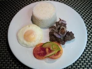 Un plato blanco con un huevo y algo de comida. en Villa Verde Guest House en General Santos