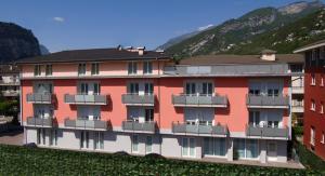 un edificio rosso con balconi e montagne sullo sfondo di Hotel Garnì Corallo a Torbole