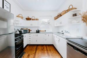 a white kitchen with wooden floors and white cabinets at Mortimer Cottage - A Pool Oasis in Heart of Mudgee in Mudgee