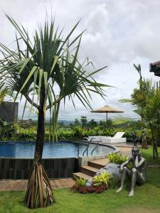 une statue d'un homme assis sous un palmier à côté d'une piscine dans l'établissement Sawah Tamanan Villa & Resort, à Yogyakarta