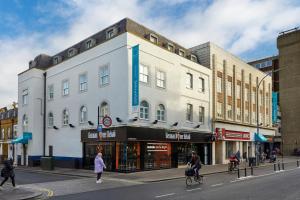 un grande edificio bianco in una strada cittadina con persone che attraversano la strada di Seraphine Hammersmith Hotel a Londra