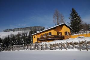 a yellow house in the snow next to a fence at Sulamith Ferienhaus mit Garten in Sankt Kathrein am Offenegg