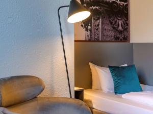 a room with a bed and a lamp and a chair at Mercure Hotel Hannover City in Hannover
