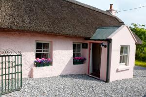 a cottage with a thatched roof and flowers in the window at Killee Cottage in Mitchelstown
