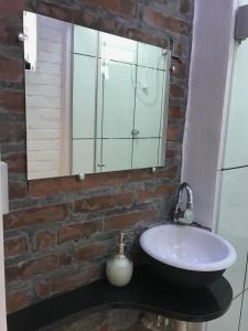 uma casa de banho com um lavatório e um espelho numa parede de tijolos em St. Virginia’s em Gramado