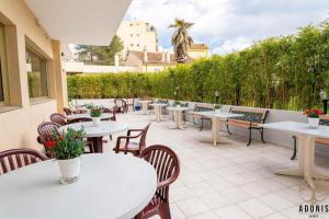 un patio con mesas blancas, sillas y plantas en Adonis Cannes - Hôtel Thomas, en Le Cannet