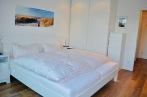 a white bedroom with a white bed with a painting on the wall at Buhne 10 App Nr 26 max 2 Pers in Dierhagen +6 photos