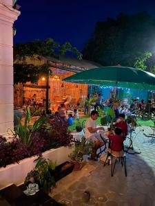 un grupo de personas sentadas en una mesa bajo un paraguas en Bloom Garden Bed & Breakfast, en Siem Reap