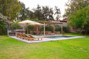 a pool with benches and tables and an umbrella at Casa de Campo La Escondida in Chincha Baja