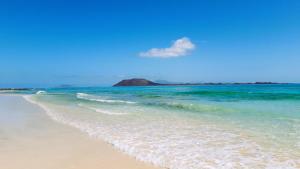 a beach with the ocean and a rock in the background at Casa Contento by Sea You There Fuerteventura in Corralejo