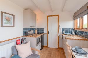 a kitchen with white cabinets and a blue tiled wall at Outbak Shepherds Hut in Cheltenham