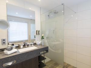 uma casa de banho com um lavatório e uma cabina de duche em vidro. em Concorde Hotel am Leineschloss em Hanôver