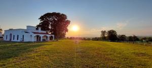 a white building in a field with the sunset in the background at CASA QUINTA LA ENCANTADA in San Miguel de Tucumán