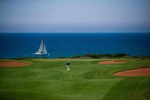 a man standing on a golf course with a sailboat in the ocean at The Westin Resort, Costa Navarino in Romanu