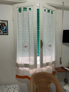 una camera con due finestre con tende bianche e una sedia di Giuly's Room a Porto Santo Stefano