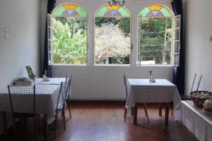 a dining room with two tables and three windows at Pousada Villa Real in Sabará