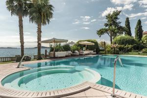 a swimming pool with palm trees and a body of water at Hotel Villa Capri in Gardone Riviera