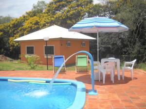 uma piscina com um guarda-sol, uma mesa e cadeiras em Pousada Chácara Mamma Gaia em Foz do Iguaçu