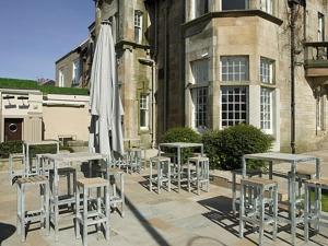 een groep tafels en stoelen met een paraplu bij Orchard Park Hotel in Giffnock