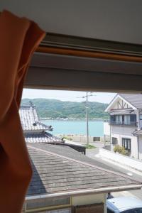 eine Person, die aus einem Fenster auf das Wasser blickt in der Unterkunft Ryokan Warajisha - Vacation STAY 62566v in Goto