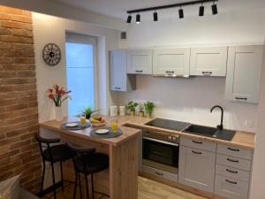 kuchnia z białymi szafkami oraz drewniana wyspa z krzesłami w obiekcie Nieborowska Loft - stylish apartment w Gdańsku