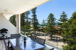 uma varanda com mesa, cadeiras e árvores em Luxury Manly Beachfront Apartment em Sydney