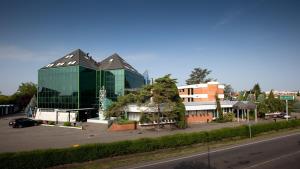 un gran edificio de cristal en un aparcamiento junto a una calle en Hotel & Loisir Le Ruote en Roveleto