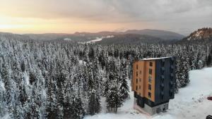 un edificio nella neve accanto a una foresta di alberi di Apartmani Snowflake a Jahorina