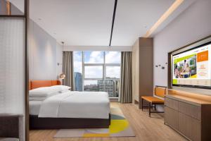 Home2 Suites By Hilton Wuhan Xudong في ووهان: غرفة فندقية بسرير وتلفزيون بشاشة مسطحة