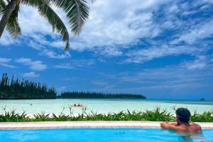 a man sitting in a swimming pool looking at the ocean at Le Méridien Ile des Pins in Oro Bay