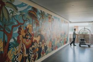 a person walking past a large mural in a hallway at Anja Jimbaran in Jimbaran