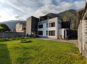 una casa blanca con un patio verde con montañas al fondo en Elegante apartamento con vistas al volcán Tungurahua, en Baños