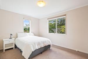 a white bedroom with a bed and two windows at Bold Beauty - Paraparaumu Upstairs Holiday Unit in Paraparaumu