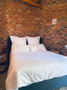 a bed with white sheets and pillows against a brick wall at Birch stay in Kempton Park +15 photos
