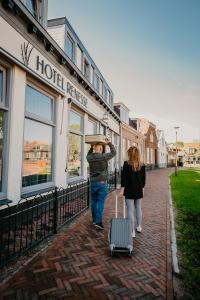 a man and a woman walking down a street with a suitcase at Hotel Renesse in Renesse