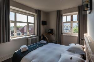 a bedroom with a bed with two pillows and two windows at Hotel Bonne Auberge (Adults Only) in De Haan