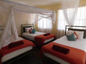 Habitación con 3 camas con sábanas rojas y blancas. en Tsumkwe Country Lodge, en Tsumkwe