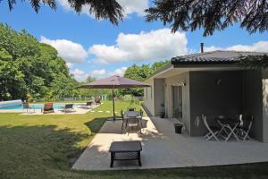 un patio con sombrilla, sillas y piscina en Les cypres, en Magnac-Bourg