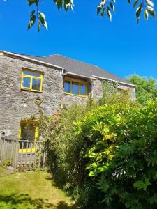 uma casa de pedra com janelas amarelas e arbustos em The Barn em Saltash