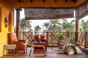 a porch with chairs and a table and palm trees at Mansa Musso Treehouse Resort in Sanyang