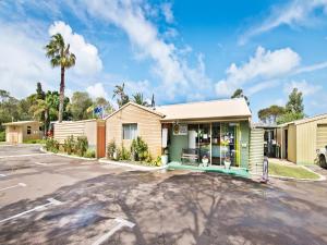 a store in a parking lot with a palm tree at Acclaim Pine Grove Holiday Park in Esperance