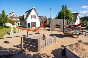 a playground in the sand with a house in the background at CLASSIC Ferienhaus Schwan A10 - a59772 in Gramkow