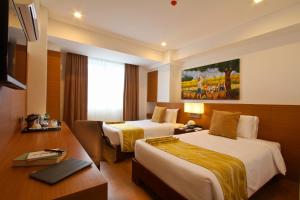 um quarto de hotel com duas camas e uma secretária em The Harvest Hotel Managed by HII em Cabanatuan