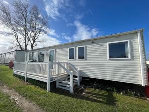 a white mobile home with a porch on the grass at Bittern 8, Scratby - California Cliffs, Parkdean, sleeps 8, free Wi-Fi, pet friendly - 2 minutes from the beach! in Scratby