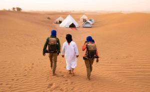 three people walking through the desert with a tent at Desert life in Mhamid