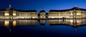 un grande edificio con luci sull'acqua di notte di Magnifique Appartement avec climatisation en Hyper Centre de Bordeaux a Bordeaux